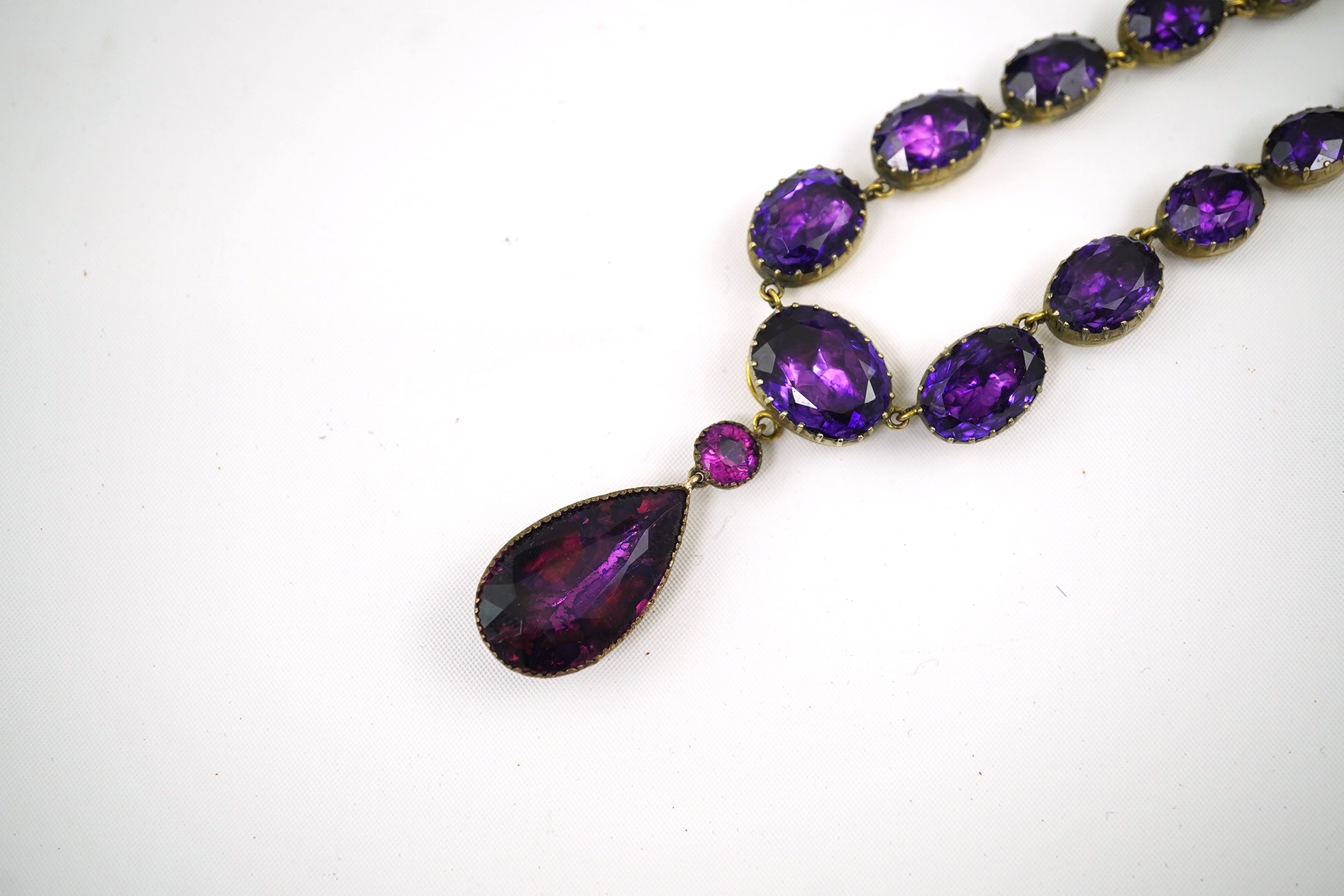 A Georgian gilt metal and graduated foil backed oval cut amethyst paste set riviere drop necklace